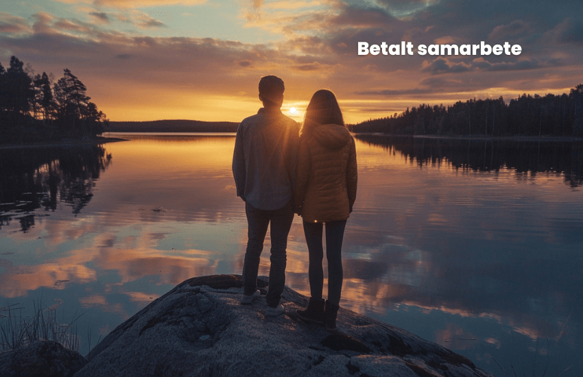 Ett par står på en sten vid en lugn sjö och tittar på en färgglad solnedgång med orange och lila nyanser. Himlen reflekteras på vattnet. Träden syns i bakgrunden. Texten "Betalt samarbete" finns i det övre högra hörnet.